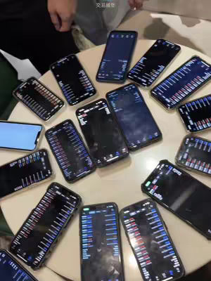A top-down shot shows multiple smartphones arranged in a circular pattern on a light-colored circular table. Each phone displays a trading interface with graphs and charts. The phones are held by unseen hands positioned around the table.