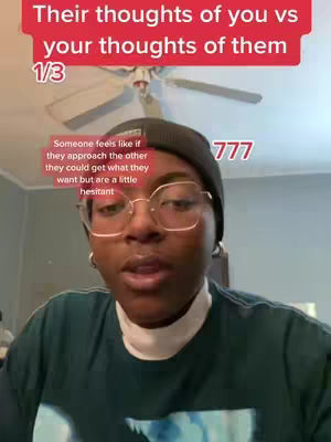 A person with glasses, wearing a black beanie and a green shirt is the focus. Text overlays are present in red, and a window fan is visible in the background.