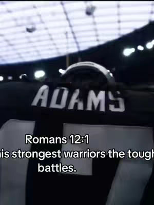 The image shows a football player's jersey from the back. The word "ADAMS" in white is seen on the back of the jersey. Below the name, white text provides a bible verse overlay. The scene is set in a stadium, with the top of the stands visible and overhead lighting in the background.
