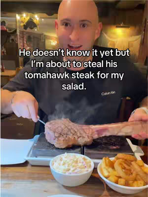 A bald man with a surprised expression sitting at a table with a tomahawk steak in front of him and text overlayed on the image.