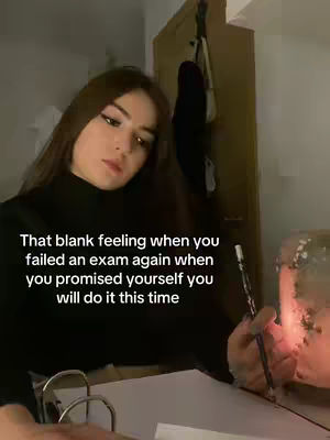 A young woman sits at a desk, holding a pen over a notebook. The background is dimly lit and features a wooden door and a softly glowing light source. Text overlayed on the image reads, 'That blank feeling when you failed an exam again when you promised yourself you will do it this time'.