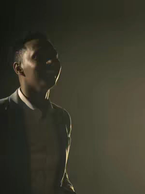 The cover image shows a man with short hair in a suit, looking slightly upward and to the side. The lighting is dim, creating a lot of shadows, and the background is a gradient from dark to light with a slight yellow or orange glow.