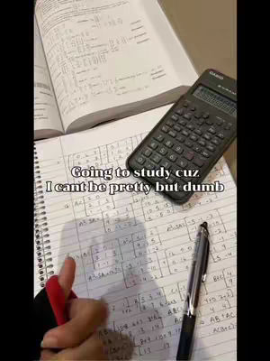 A top-down shot of a student's desk. There's an open textbook with formulas, a calculator, a notebook with handwritten math equations, a pen, and a hand with a red nail. The hook text overlayed says 'Going to study cuz I can't be pretty but dumb'.