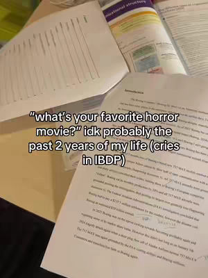 The cover image shows a desk or table with what appears to be papers, books, and notebooks scattered across its surface. Two main text elements are overlaid with the question, "What's your favorite horror movie?" followed by the phrase "idk probably the past 2 years of my life (cries in IBDP)."