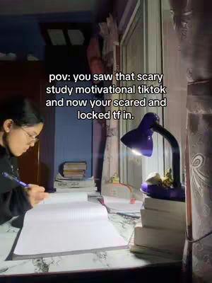 A young woman is sitting at a desk, working on a school task at night. The frame is dark, lit by a lamp above her. Text is overlaid in the center of the image.
