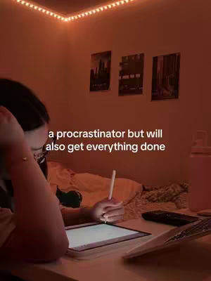A person is shown in a dimly lit room, illuminated by warm, orange-toned string lights. The person is seated at a desk, with a tablet resting on the desk surface. The person is holding a stylus and looking at the tablet. The text overlay reads, \"a procrastinator but will also get everything done\"