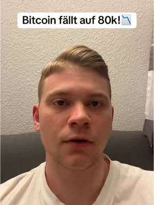 A close-up shot of a man looking toward the camera with a text overlay that reads 'Bitcoin fällt auf 80k!' in a white box at the top. The man is in a room, possibly a home, with a plain wall as the backdrop.