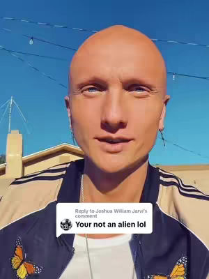 The cover image features a close-up of a man with a shaved head and fair skin against a vivid blue sky. He's wearing a black and beige jacket with butterfly illustrations. A comment box on the image says, "Your not an alien lol". The composition is straightforward, focusing directly on the man's face and the surrounding environment.