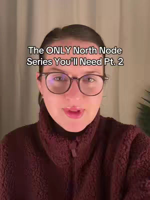 A woman with glasses is centered in the shot, facing the camera directly. She's wearing a maroon sweater and has text overlayed above her head. The background seems to be a neutral color, likely a wall or curtains.