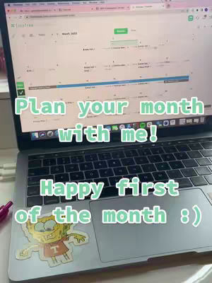 A laptop screen is the focal point, displaying a calendar from an app called TimeTree. Overlayed on the image are green and white text boxes with the phrases "Plan your month with me!" and "Happy first of the month :)". A sticker of a cartoon character is on the laptop's surface.