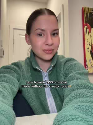 A woman with fair skin is centered in the frame, gazing directly at the camera. She has brown hair pulled back, with a simple center part. The woman's rosy cheeks and neutral makeup enhance her features. She wears a green, textured fleece jacket, zipped up most of the way, suggesting a casual, indoor setting. Behind her are muted white walls and a glimpse of closed white doors. The overall composition is straightforward, with the focus on the woman and her message.