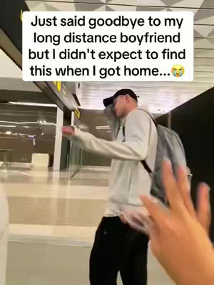 A man in a light gray hoodie and black pants is shown walking in an airport with a backpack. A text box in the top left corner states, "Just said goodbye to my long distance boyfriend but I didn't expect to find this when I got home..." The image has a blurry background that doesn't distract from the subject.
