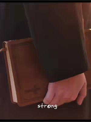 The image shows a person's hand holding a brown book, possibly a Bible. The hand is partially visible, and the book is held at an angle. The background is blurred, suggesting the focus is on the book and the hand. There is a text overlay at the bottom that reads 'strong'.