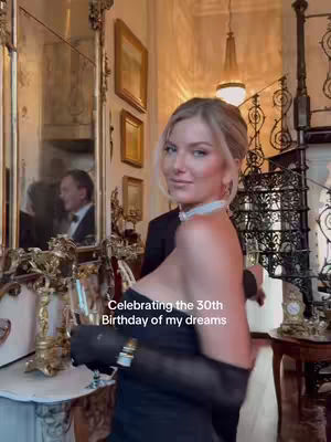 A woman in a black dress and gloves is posing for the camera in a well-lit, ornate room. Behind her is a large mirror, reflecting a man in a tuxedo, and antique furnishings. The text overlay emphasizes the celebration of a 30th birthday.