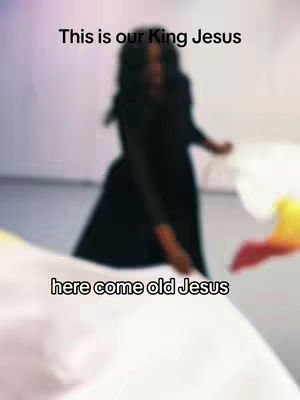 The blurred image shows a person, likely a woman wearing a black dress, in front of a soft, light-colored backdrop. White and yellow fabrics are held or waved in the foreground, creating a sense of movement and worship.