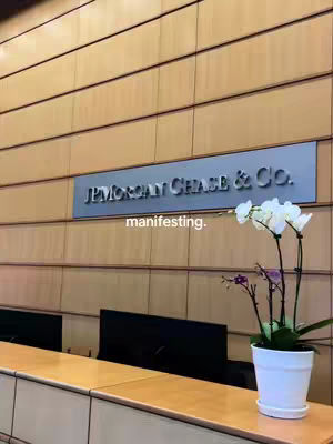A photo shows the interior of a building, with a sign for J.P. Morgan Chase & Co. overhead. In the foreground, there's a wooden desk or counter, with a white pot of orchids to the right.