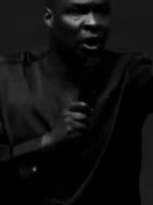 The cover image features a man in a dark setting, likely indoors, speaking into a microphone. The shot is close-up, focusing on his face and upper body, with a slight tilt. The background is dark, and the man is wearing a dark shirt or jacket. The overall tone is serious, as if he is delivering a message or a speech, the light is very neutral.