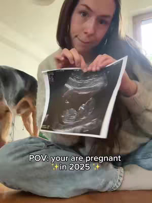 A young woman holds an ultrasound image, with text overlaid at the bottom. A dog is partially visible on the left side of the frame.