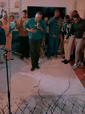 A group of people are standing on a light-colored rug, and a man with a microphone in his hand is the central figure.