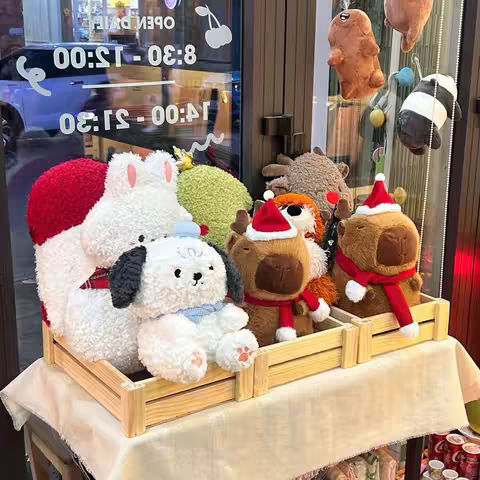 A display of various stuffed animal characters, including a white bunny with red accents, a white dog with blue accessories, and brown reindeer with Christmas hats and scarves, all within wooden crates. The background shows a shop interior with glass windows, a clock displaying time, and text overlays.