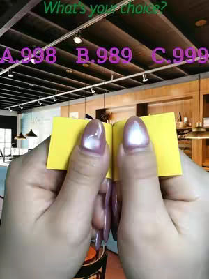 A person holding two yellow sticky notes, angled open, revealing the inside of their nails with a background showing an indoor ceiling with track lighting. The text "What's your choice?" is in green while the options are in purple: A.938 B.989 C.999.