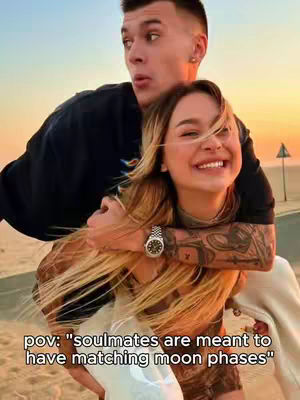 A couple embraces on a beach at sunset. The woman, in focus, smiles widely with long blonde hair. The man stands behind her, arms around her, with a surprised expression. Text overlay at the bottom.