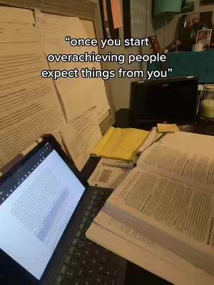An overhead shot of a desk covered in papers, books, and a laptop. Text overlayed on the image reads a motivational quote.