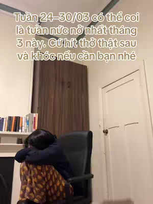 The cover image shows a person sitting in a chair with their head resting on their arms. The background includes a wooden wardrobe, a wall, a door, and a bookshelf. The text overlayed on the image states, "Tuan 24-30/03 co the coi la tuan nuc no nhat thang 3 nay. Cu hit tho that sau va khoc neu can ban nhe".