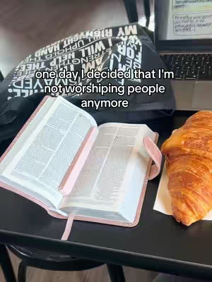 A coffee shop scene with an open Bible, croissant, and a laptop. Text overlay reads a quote about not worshipping people. The scene is warm lit.