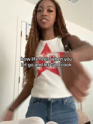 A young woman with long, braided hair, wearing a white t-shirt with a red star design and blue jeans, is captured in a selfie against a light-colored background. The text overlay states a positive message about faith.