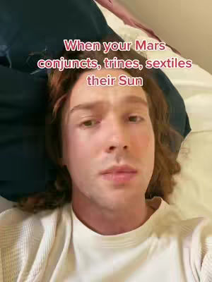 A man with reddish-brown hair is lying on a bed, looking at the camera. Text overlayed in the image reads, "When your Mars conjuncts, trines, sextiles their Sun."
