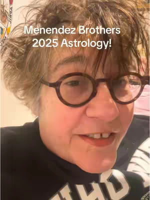A close-up shot of a person wearing glasses. The subject has short, tousled brown hair and is wearing dark-rimmed glasses. The person is looking towards the camera with a slight smile, and a black shirt is visible. Overlaid on the image is the white text "Menendez Brothers 2025 Astrology!" in a sans-serif font.