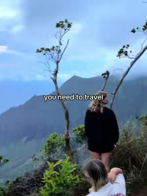 The image shows a scenic overlook with a blurred foreground featuring a woman's hair and a second woman's back in a white shirt, while the background features a scenic view of mountains with the text overlayed.