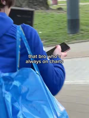 A person is walking in an outdoor setting, viewed from the back and partially visible. The person, dressed in blue, is holding a smartphone and carrying a large blue tote bag over their shoulder. The scene suggests a casual, everyday moment, with a muted color palette dominated by blues and greens.