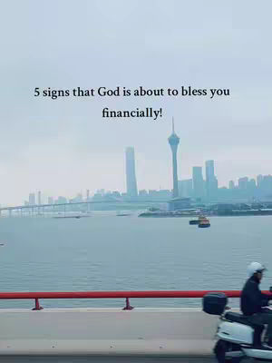 A shot from a moving vehicle, with a cityscape including bridges and tall buildings, and a motor scooter in the right foreground. Text overlayed mentions signs that God is about to bless financially.