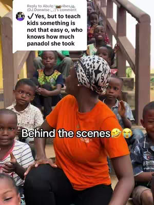 The cover image shows a group of children and a woman, possibly a teacher. The woman, wearing an orange shirt and a patterned head covering, is the focus, with the children in the background. She appears to be looking at the children. The text overlay indicates a behind-the-scenes look at the interaction, suggesting a humorous or challenging aspect of teaching.