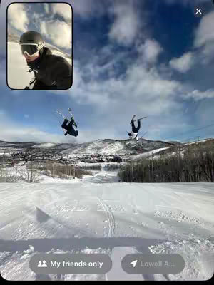 The cover image shows two skiers in mid-air, performing flips against a backdrop of a snowy mountain landscape and a partly cloudy sky. In the top left corner, there's a smaller framed inset showing a selfie of the creator in ski goggles and a helmet. The overall composition captures action and incorporates social media framing.