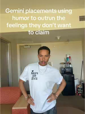 A man wearing a white t-shirt with text stands in an apartment, posing and looking directly at the camera. There is additional text at the top of the image.