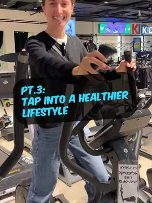A woman is standing on an eliptical machine in what looks like a fitness equipment store/shop. The woman is smiling at the camera and is wearing a black sweater, a white shirt, and blue jeans. Text is overlaid on the image.