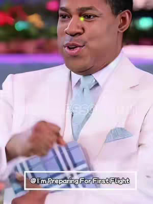 A man in a white suit is speaking, holding a gift. The background is blurred, suggesting a stage or studio setting. A text box at the bottom reads "@ I'm Preparing For First Flight".