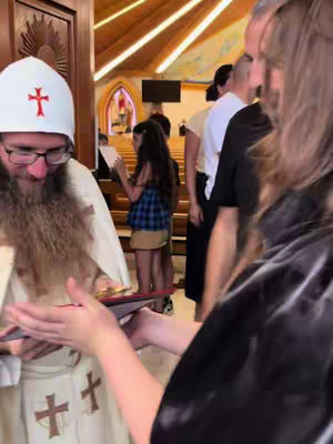 The image captures a moment inside a church, featuring a man in religious attire holding a book and interacting with someone, likely handing it over. Several individuals are present, suggesting a gathering or event. The lighting is bright, highlighting the details of the interior and the people involved.