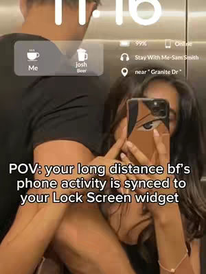 A selfie-style shot in an elevator. A woman is holding the phone to capture both her and a man's face. The lock screen of a phone is visible in the background with status updates showing time, battery life, and location. The woman is wearing an outfit.