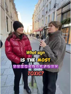 Two people are standing on a street in an urban setting. The person on the left is wearing a red puffer jacket and a black beanie. The other person is next to them wearing a light brown jacket and holding a microphone. Both are facing each other in conversation with a text overlay on the bottom of the image.
