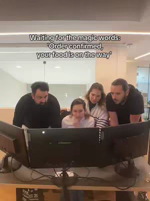 Four people are gathered around a computer screen in an office setting. They are looking intently at the screen, with the text overlay at the top.