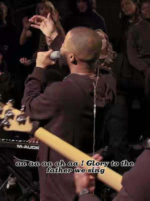 The cover image shows a man in a maroon hoodie singing into a microphone. He is the central figure, with his head shaved. The background is dimly lit, showcasing a choir or musical group.