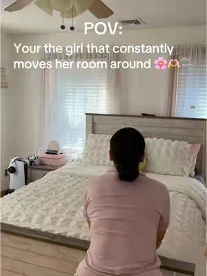 The image captures a bedroom scene from a first-person perspective. A person, seen from the back with dark hair in a bun faces toward a bed with white bedding. The room is well-lit, with a ceiling fan above and curtains framing a bright window. Text overlays the scene, setting a POV context.