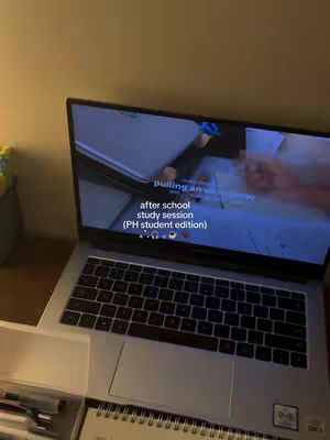 A laptop is partially open on a desk, displaying a screen with text and graphics. A notebook and pens sit in the foreground. The image has a warm, inviting color scheme.