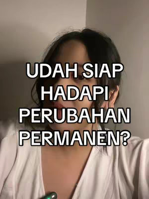 A medium close-up shot of a person with dark hair framing the face. The person is wearing what appears to be a white shirt or top. Overlayed on the image is white text in a bold, sans-serif font. The background is a blurred neutral tone.