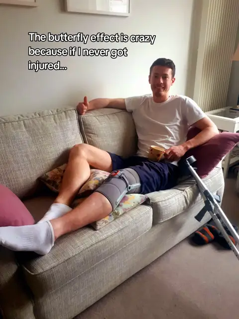 A man is seated on a beige couch with his leg elevated on pillows and braced with a knee support. He's smiling and giving a thumbs-up. Text overlay adds a caption.