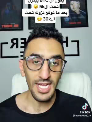 A man with glasses is speaking directly to the camera, with text overlays in Arabic. The background includes framed pictures and a logo. The image has a warm, inviting feel.